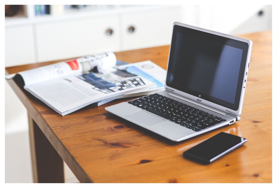 Photo of a notebook, laptop, and cell phone on a desktop.